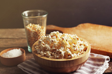 Salted popcorn in a bowl on stripped napkin with board and glass of corns on wooden table