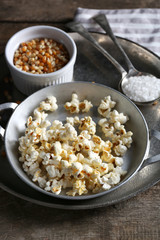 Salted popcorn in a metal bowl with cup of corns on wooden table
