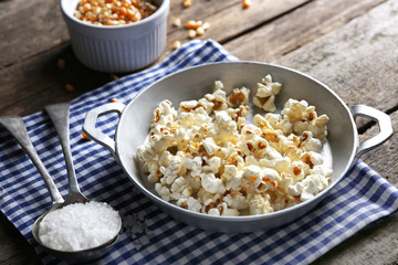 Salted popcorn in a metal bowl with cup of corns on checked cotton napkin on wooden table