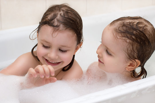 Two adorable little girls taking a bath with soap suds