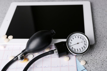 Blood pressure meter, stethoscope, digital tablet on gray background
