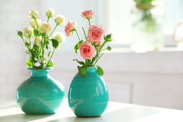 Beautiful roses in turquoise vases on window background