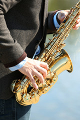 Young man playing on saxophone on the riverside