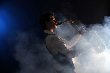 Attractive woman plays saxophone on dark background in the smoke