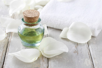 Fototapeta na wymiar Bottle of green essential oil, white rose petals and soft towel