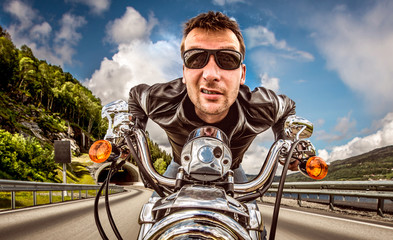 Obraz premium Śmieszny rowerzysta w okularach przeciwsłonecznych i skórzanej kurtce ściga się na górze