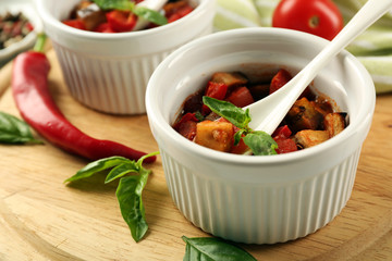 Tasty vegetarian ratatouille made of eggplants, squash, tomatoes in bowls on wooden table background