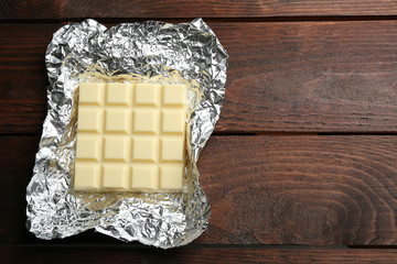 White Chocolate bar in foil, close-up, on wooden background