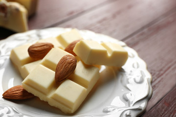White chocolate pieces with nuts on plate, on color wooden background