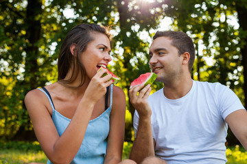 Couple sitting on a picnic blanket and eating watermelon.