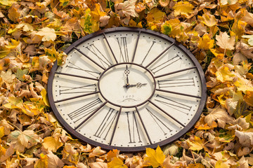 Fototapeta premium Herbstzeit - Uhr im Laub, Zeitumstellung auf WInterzeit