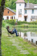 a man sitting in a chair by the lake. fisherman with a fishing rod in his hands in anticipation of the day in the summer. portrait of male Europeans.