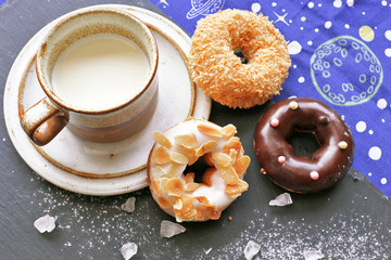 Donuts on stone board with sugar powder , crystals  and cup of milk 