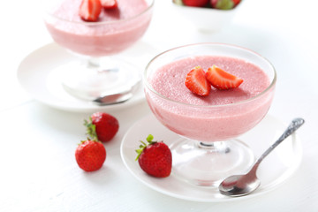 Tasty strawberry mousse in glass on white wooden table