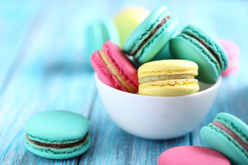 Tasty colorful macarons in bowl on a blue wooden table