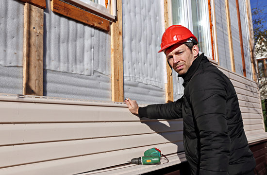 A worker installs panels beige siding on the facade