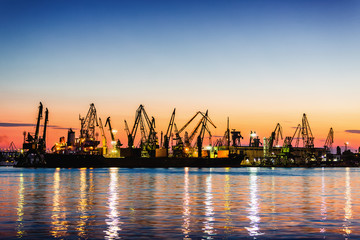 Sea commercial port and working Industrial cranes. Cargo freight ship in sea harbour at sunset....