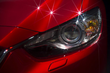 Headlight and hood of powerful sports red car with stars on bodywork, isolated on black  - 94877356