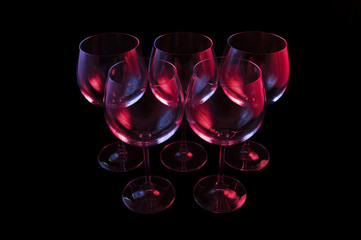 Nightclub wine glasses lit by red, blue, lilac party lights, nightlife, five object in row isolated on black background 