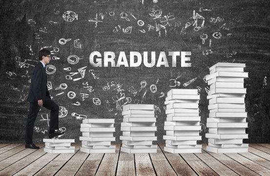 A Man Is Going Up Using A Stairs Which Are Made Of White Books. The Word Graduate Is On The Black Chalkboard. Wooden Floor.