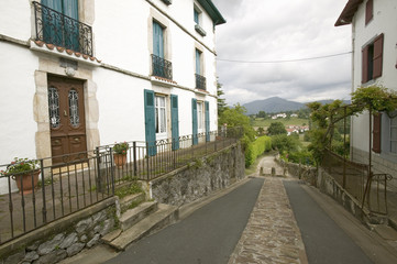 Fototapeta na wymiar Path between homes in Sare, France in Basque Country on Spanish-French border, a hilltop 17th century village in the Labourd province. The houses are built in the traditional style of the region, with shutters painted colors red and green of the Basque flag. Close to St. Jean de Luz, on the Cote Basque, France.