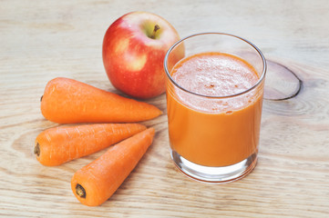 Glass of homemade juice, apple and carrot on wooden board