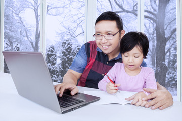 Father using laptop while helps his child studying