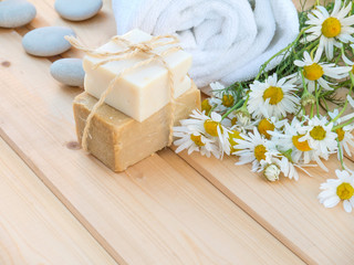 Obraz na płótnie Canvas White towel, soap bars and camomile bouquet on the natural wood