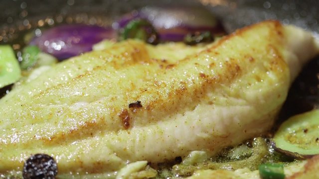 Fish fillet cooking in oil on stove top frying pan