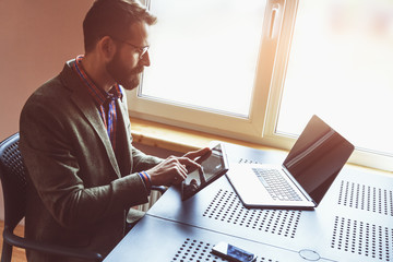 bearded man working with laptop and digital tablet in morning su