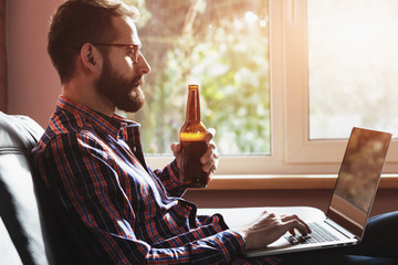 bearded man with laptop drinking bottle of beer - 94891123
