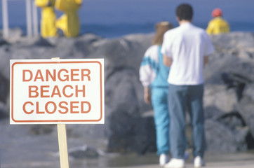 A sign warning, dangerÐbeach closed with people in the background