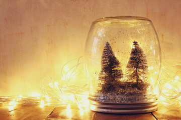 low key and vintage filtered image of christmas trees in mason jar with garland warm lights and...