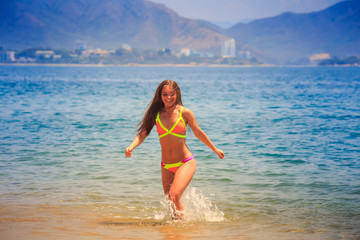 blonde slim girl in bikini runs out of azure sea water smiles