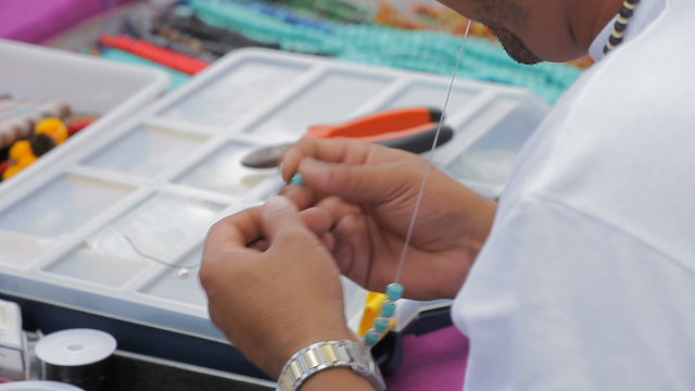 Handicraftsman making a necklace with beads on the street