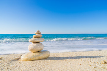 Fototapeta na wymiar Stones pyramid on sand symbolizing zen, harmony, balance. Ocean