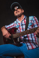senior man playing an electric guitar seated, looks up