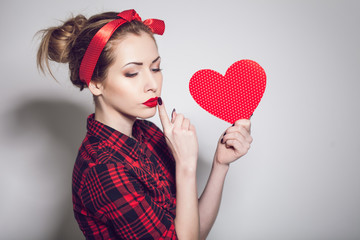 Beautiful young woman with pin-up make-up posing with red heart