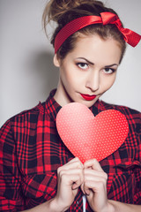Beautiful young woman with pin-up make-up posing with red heart
