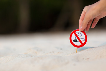 Female hand holding "No smoking" sign on the beach on white sand background