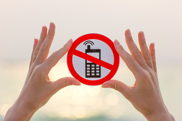 Female hands holding "No phone calls" sign on the beach on sea background