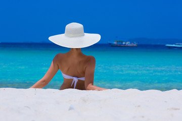 Woman in white hat lying on the beach, blue sea and sky background