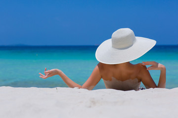 Fototapeta na wymiar Woman in white hat lying on the beach, blue sea and sky background