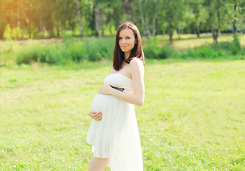 Beautiful young pregnant woman in white dress on nature