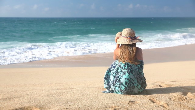 Rear View Of Blonde Woman Sitting On The Beach And Looking At The Ocean