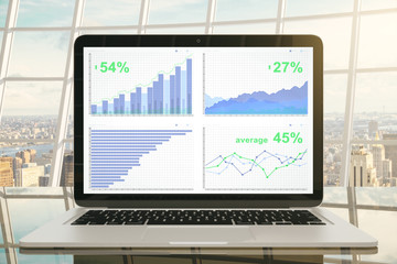 Business graph on laptop screen on glassy table in sunny office