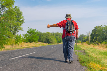Senior hitchhiker walking on a roadside in Ukrainian rural area at summer time