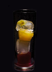 Glass of colored ice cubes isolated on black