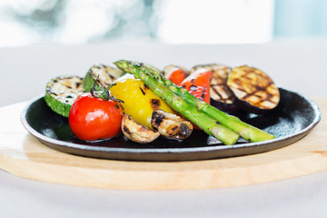 mix of tomatoes, asparagus, zucchini, bell peppers and mushrooms grilled and served on a wooden plate on a table in a restaurant