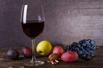 Glass of red wine, cheese, grape, walnuts, figs, plums and apple on wooden background. Still life